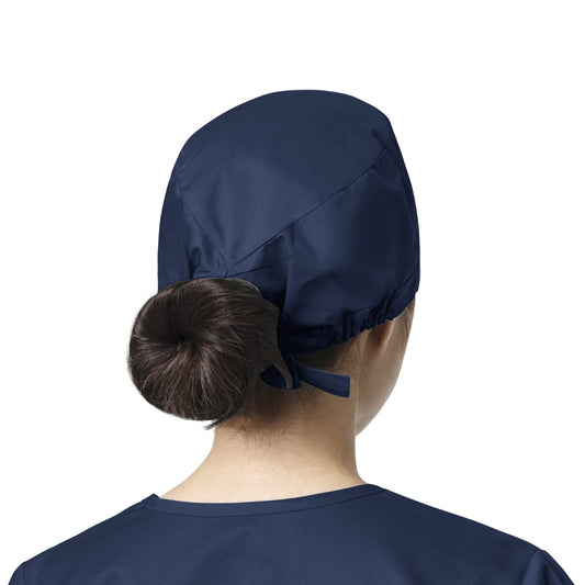 Une femme portant un calot médical WonderWink bleu marine avec un nœud, facile à entretenir