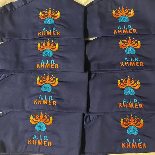 Masques faciaux bleu marine avec texte brodé 'KHMER' et logos de couronne en orange et turquoise.