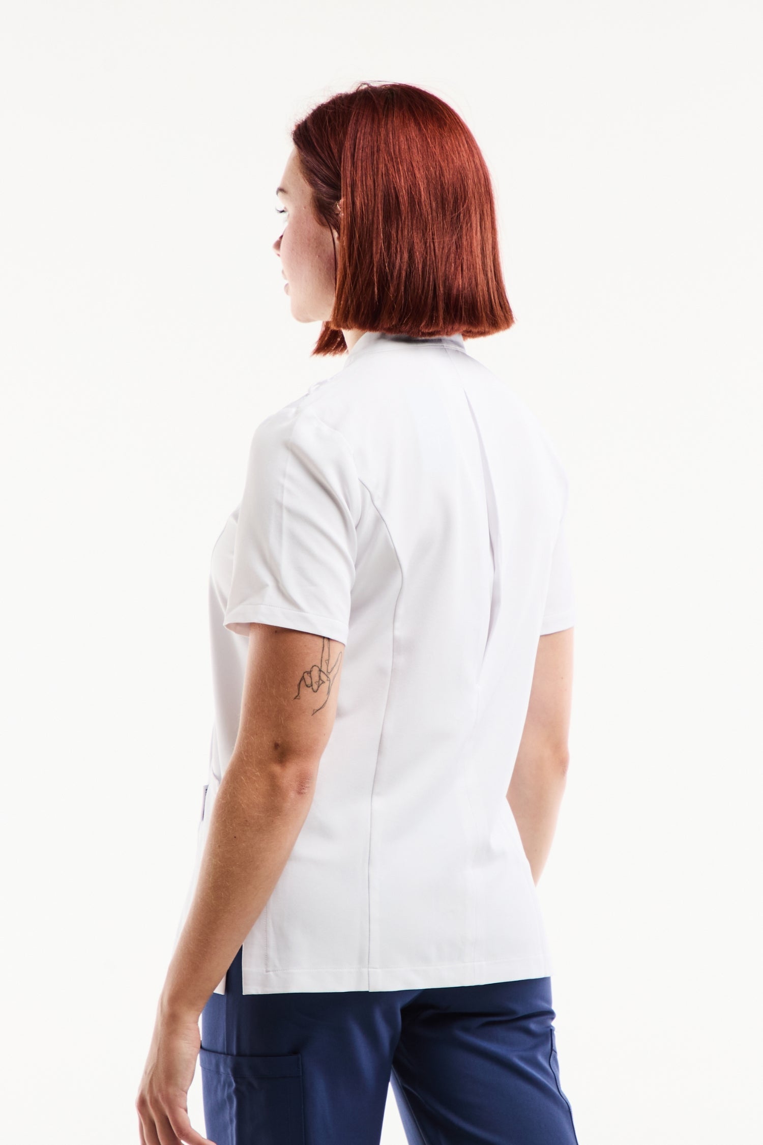Blouse médicale femme Aurelia blanche à col officier, asymétrique à pressions, avec pantalon bleu marine et tatouage