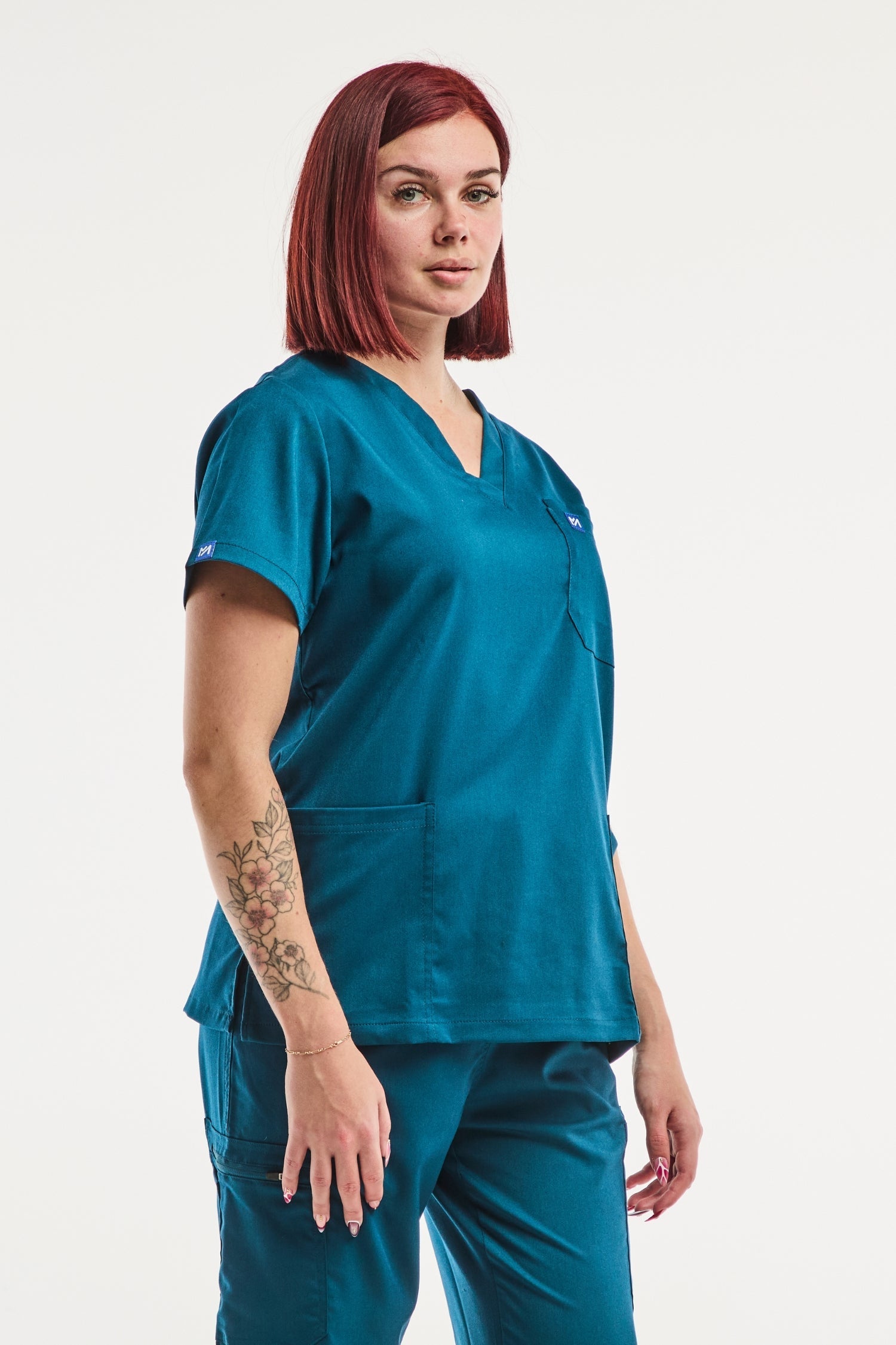 Photo d’une femme portant la tunique médicale col turquoise EMMA avec tatouage