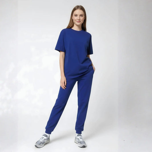 Une femme porte un ensemble assorti de haut à manches courtes bleu royal et de pantalons de jogging, assorti de baskets athlétiques argentées.