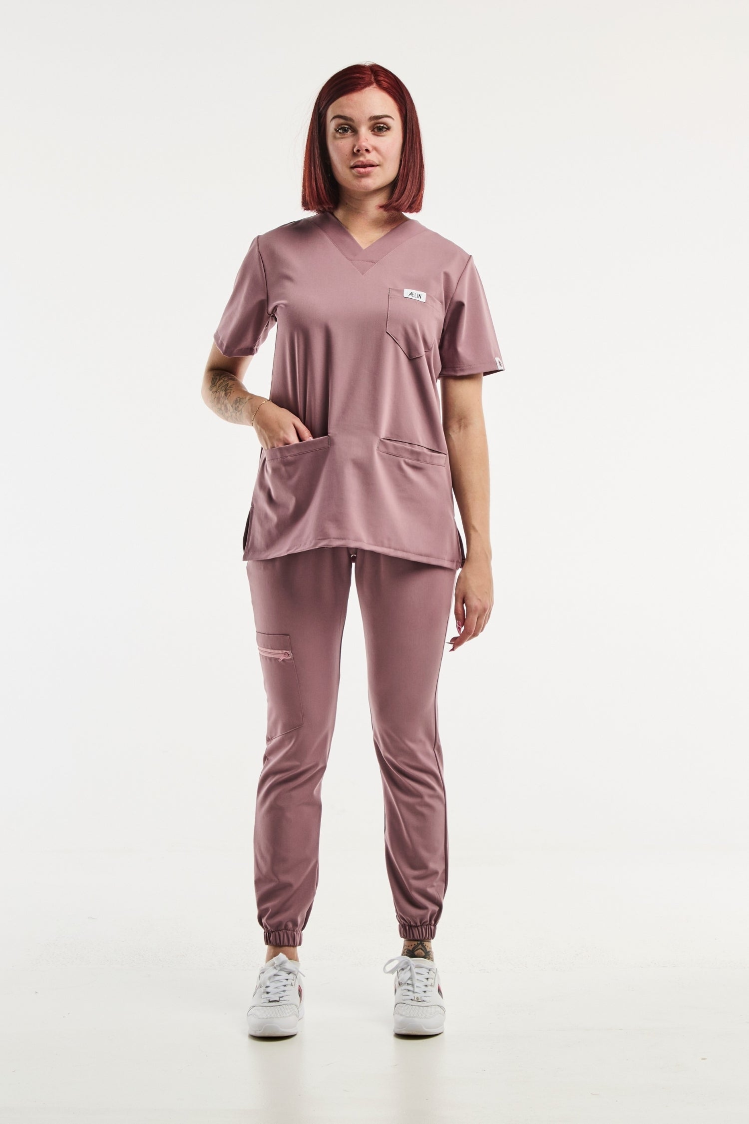 Femme en uniforme médical Slimfit New, portant des scrubs mauves élégants