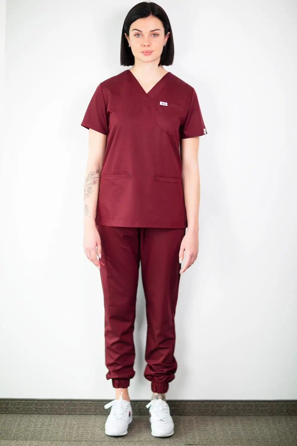 Une femme en tenue médicale bordeaux pose, mettant en valeur le pantalon médical slim fit